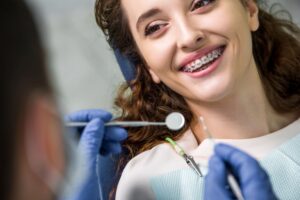 Kobieta siedzi na fotelu dentystycznym i pokazuje swoje zęby, na których znajduje się aparat