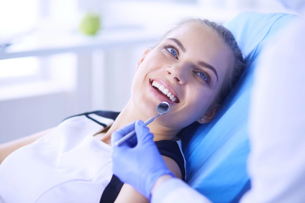 Kobieta siedzi na fotelu dentystycznym i pokazuje dentyście swoje uzębienie do sprawdzenia.