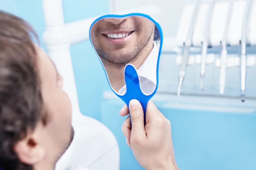 Mężczyzna ogląda swój uśmiech w lusterku dentystycznym